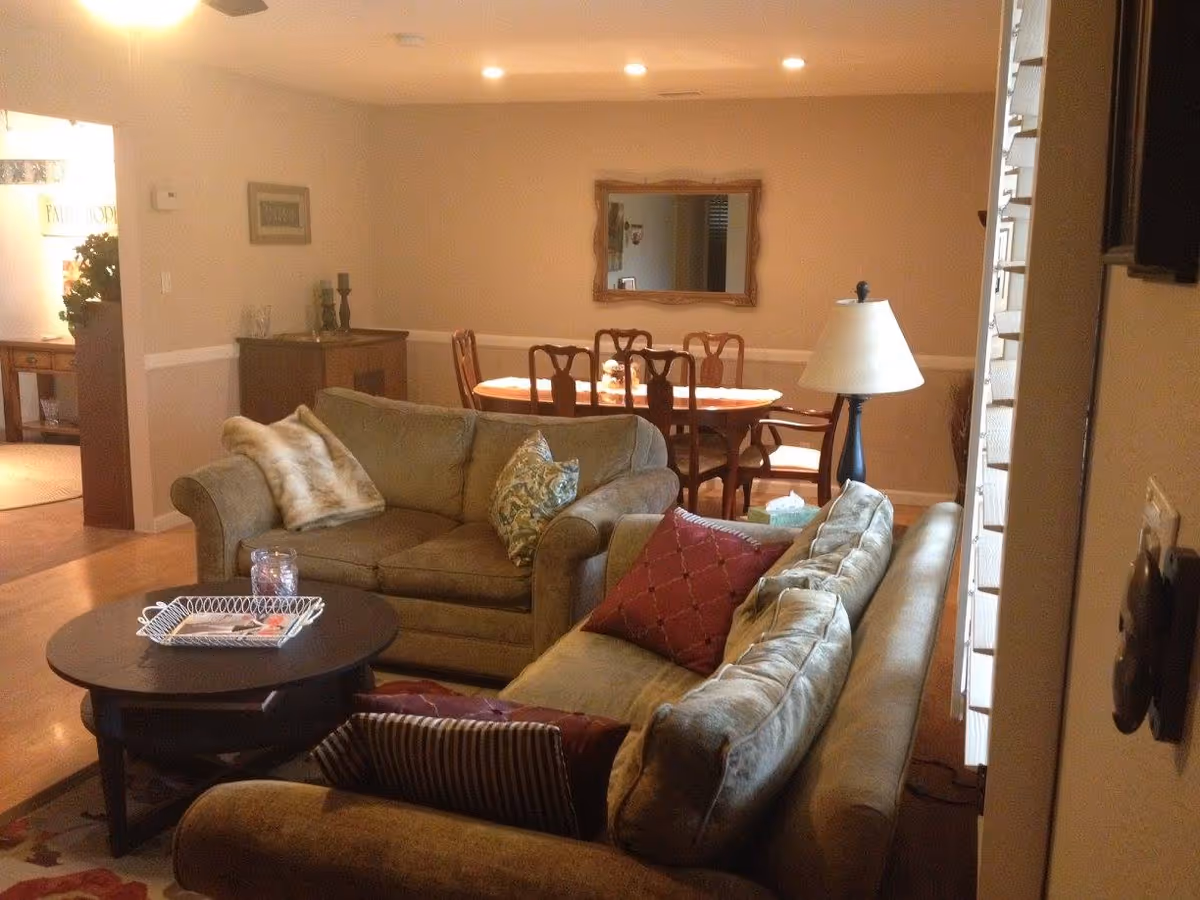 Cozy living room with two sofas and a coffee table, a floor lamp to the right, and a dining table visible in the background.