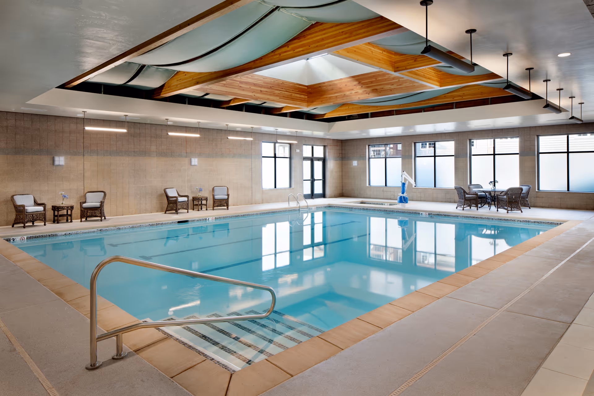 Indoor swimming pool with seating, large windows, and a decorative wood-beamed ceiling.