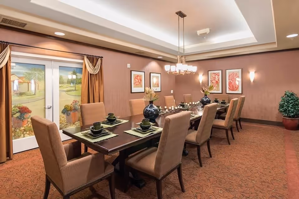 Elegant dining room with a long set table, upholstered chairs, chandelier, and decorative wall art.