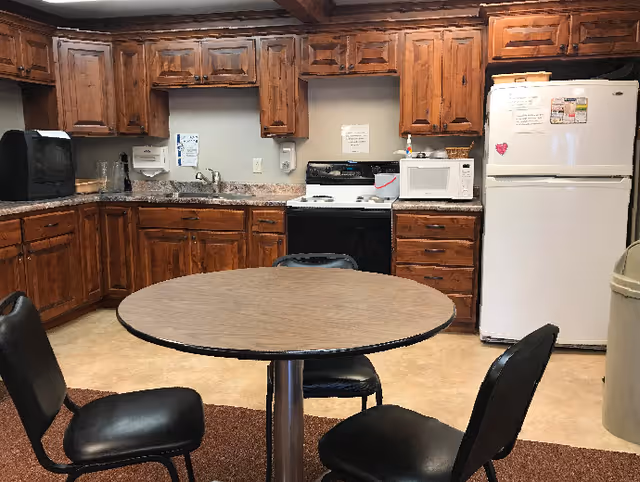 A kitchen area with wooden cabinets, a white refrigerator, a microwave, a black stove, and a round table with four black chairs around it.
