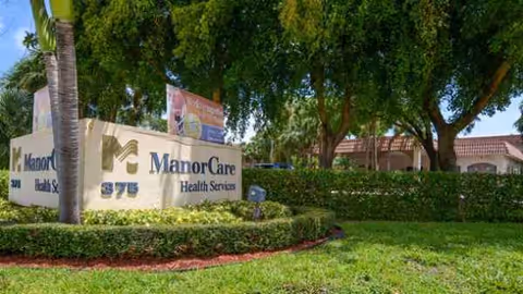 Exterior view of ManorCare Health Services Boca Raton with entrance sign and greenery.