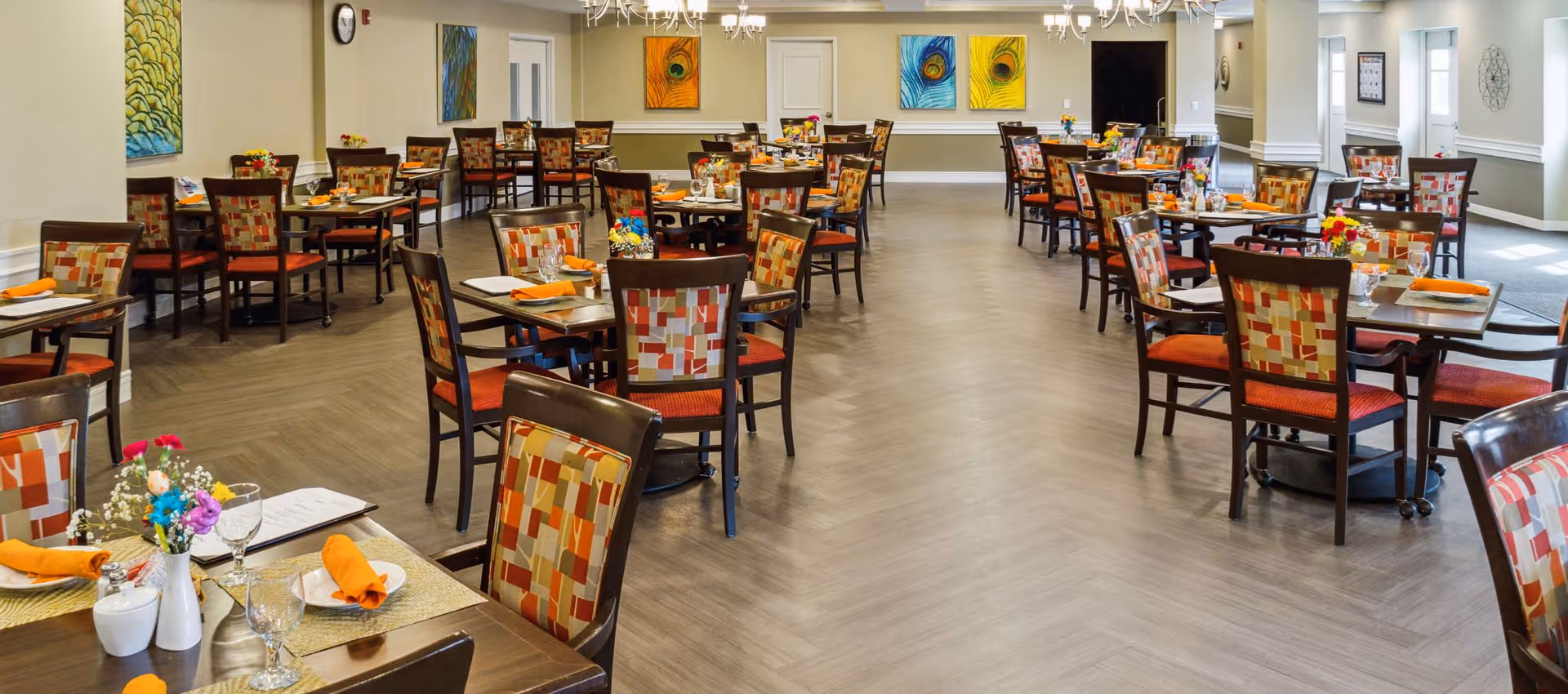 Spacious dining room with multiple tables set with orange napkins and patterned chairs.