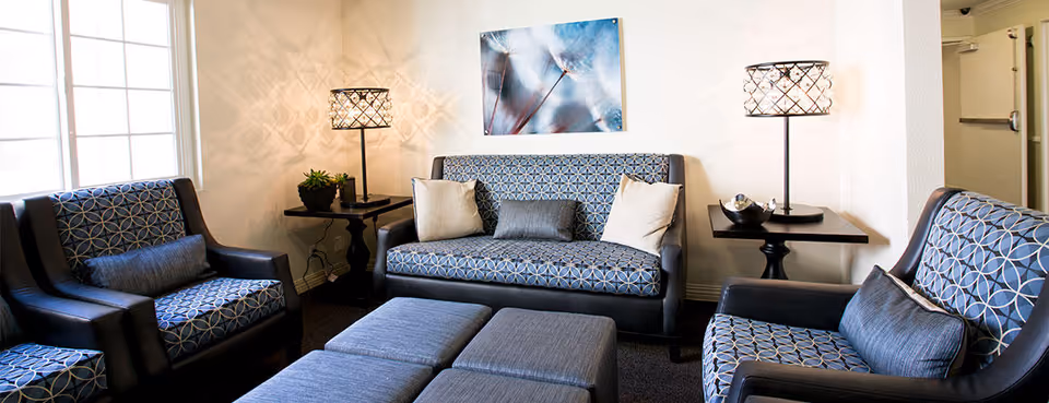 A cozy seating area with patterned armchairs and a loveseat, ottomans, side tables with lamps, and wall art.