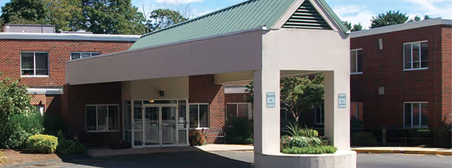 Exterior view of Southeast Rehabilitation & Skilled Care Center showing the main entrance with a covered drop-off area, surrounded by a two-story brick building and greenery.
