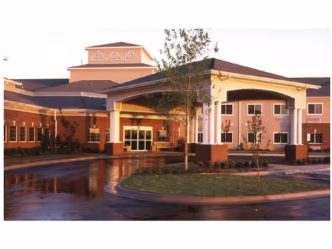 Front entrance of a senior living facility with a covered porte-cochere, columns, and a wet circular driveway.
