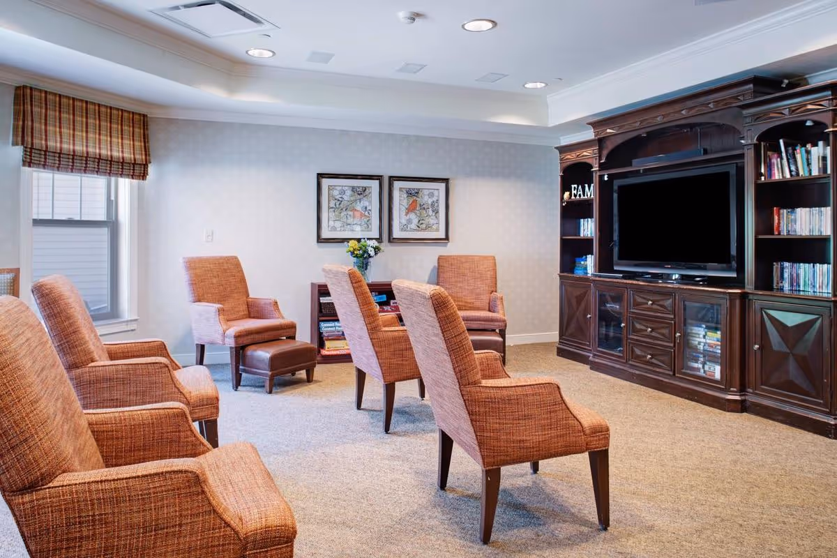 A cozy seating room with multiple upholstered armchairs arranged facing a large wooden entertainment center with a TV and bookshelves.