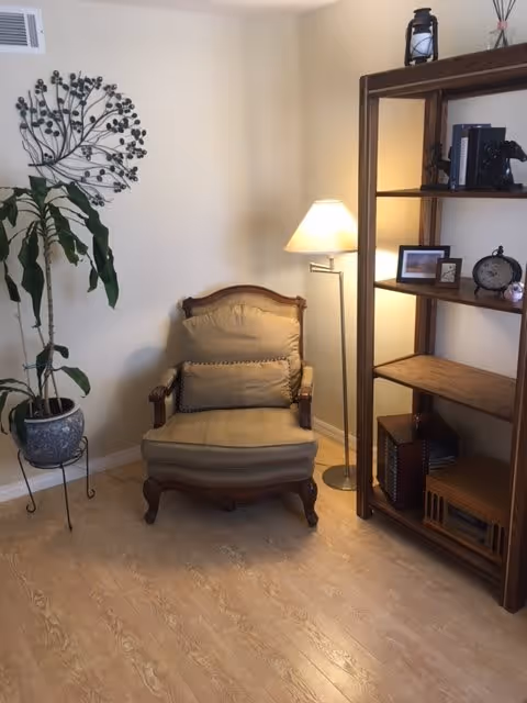 Cozy corner of a living room with an upholstered armchair, floor lamp, wooden shelving unit, and potted plant.