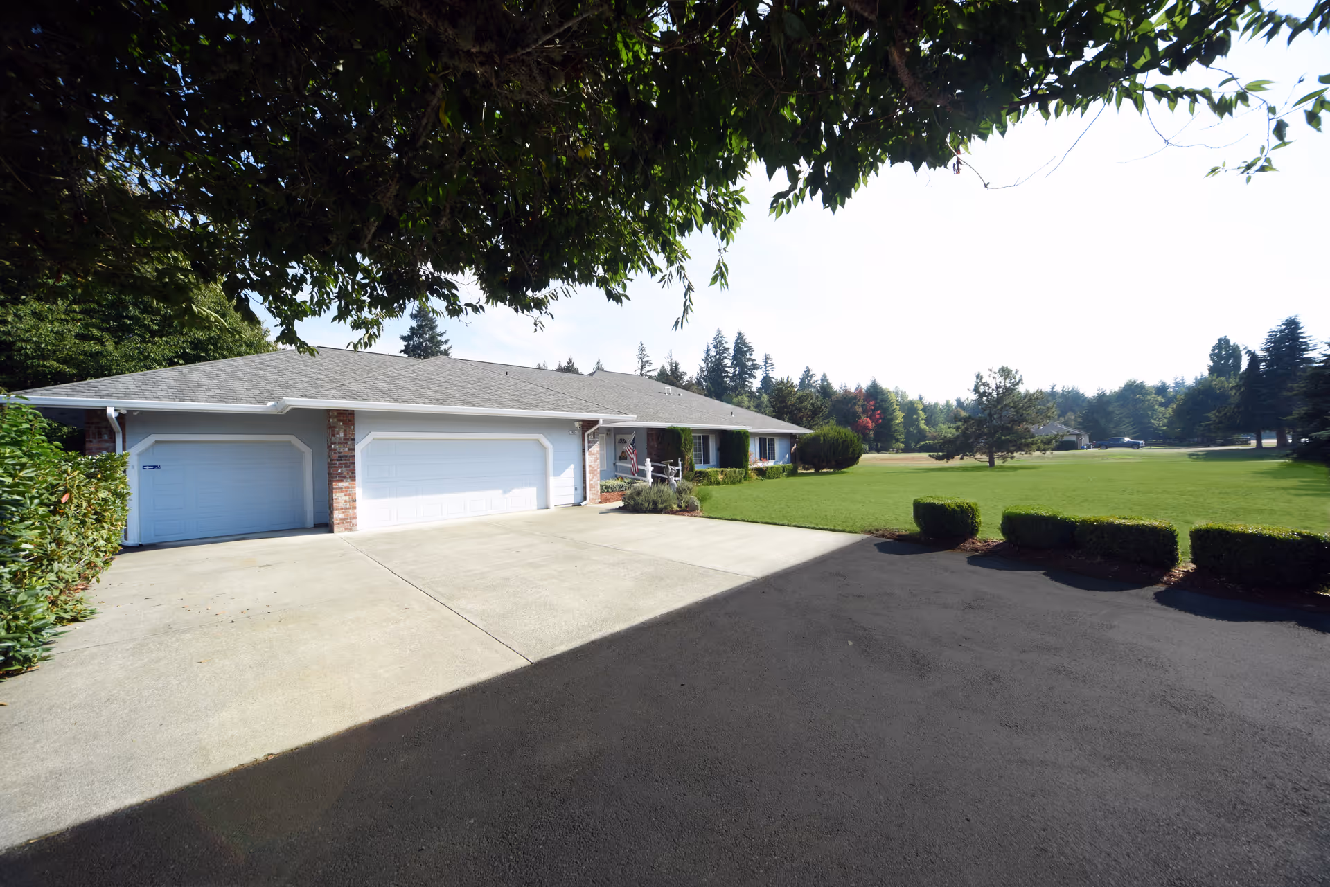 Single-story ranch-style house with a three-car garage, wide concrete driveway and expansive green lawn.