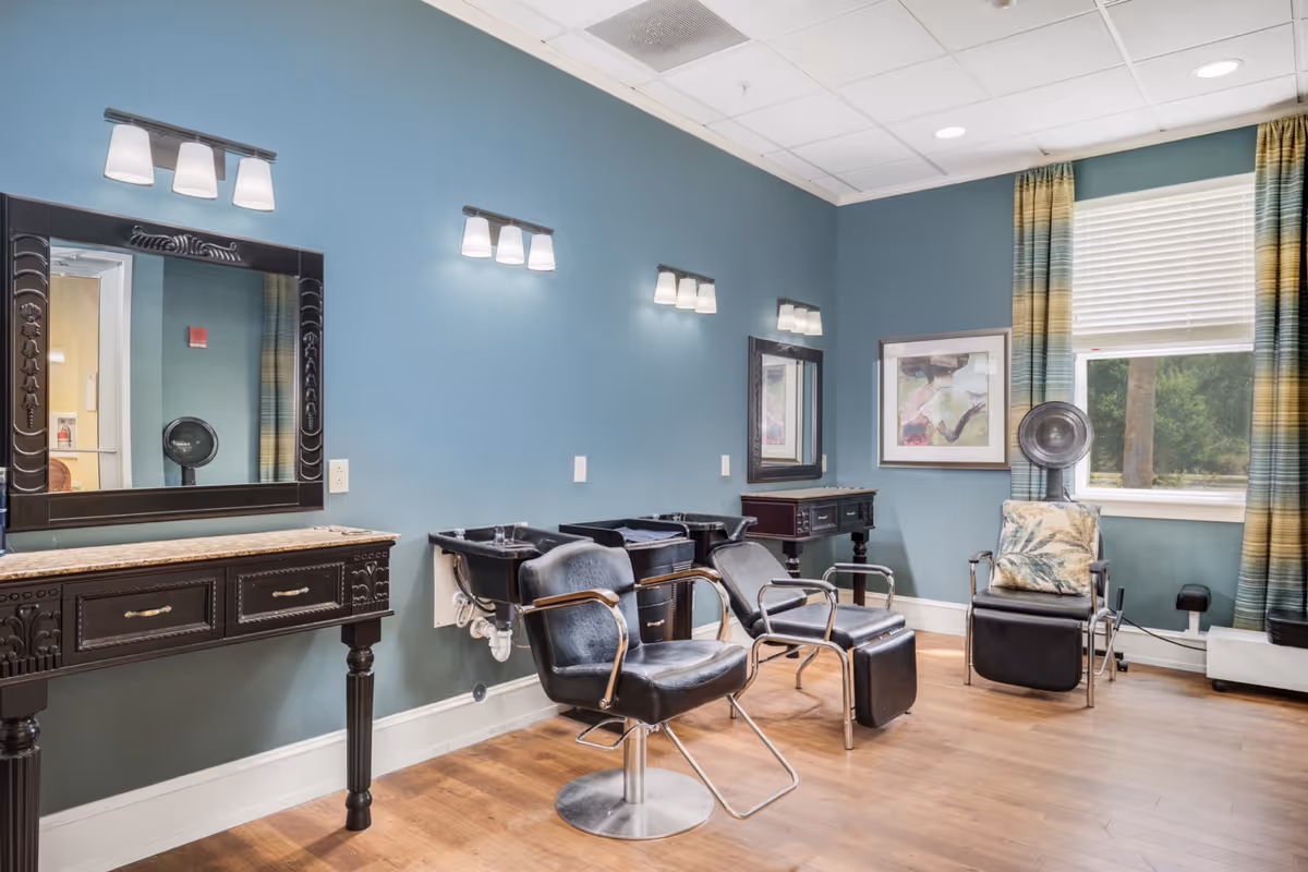 A bright salon-style room with multiple styling chairs, shampoo sinks, mirrors, and a window with striped curtains.