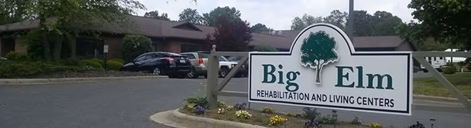 Entrance sign reading "Big Elm Rehabilitation and Living Centers" in front of a single-story building and parking lot.