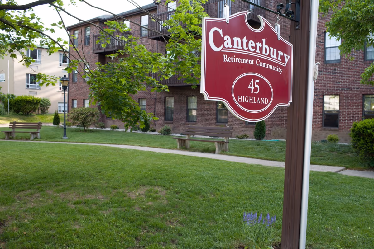 A red Canterbury Retirement Community sign reading "45 Highland" in front of a brick building and grassy courtyard with benches.