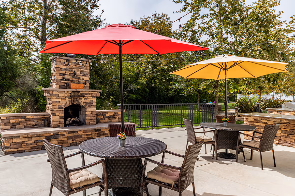 Outdoor patio with wicker tables and chairs under red and yellow umbrellas and a stone fireplace.