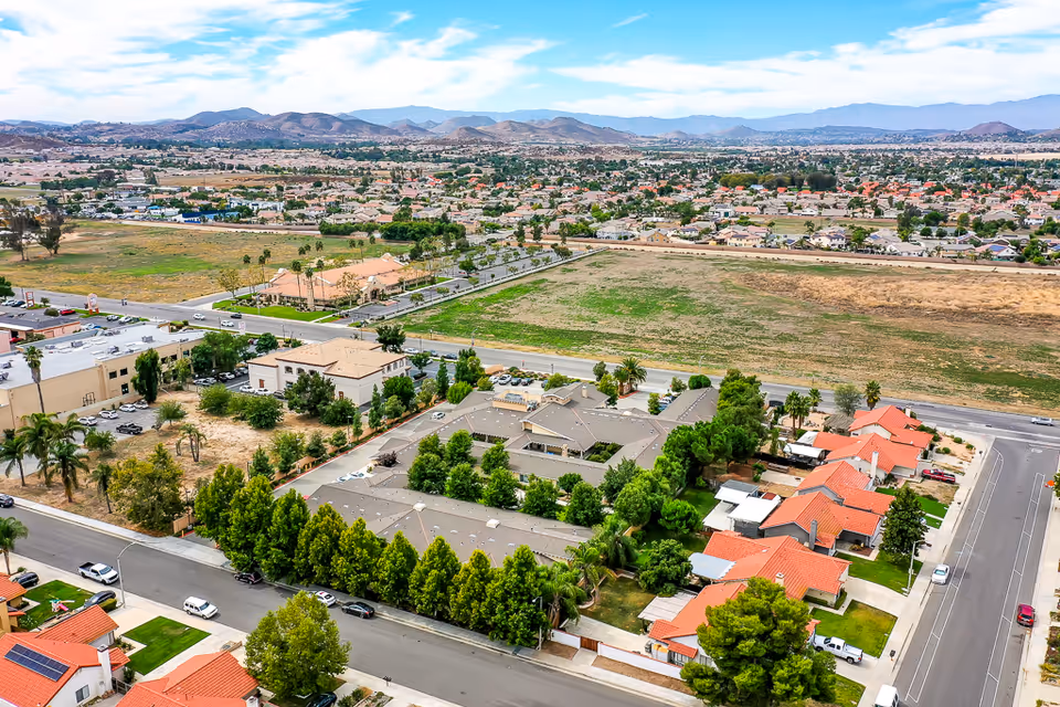 Aerial view of Sunny Rose Senior Living and surrounding suburban neighborhood with homes, streets, and open fields.