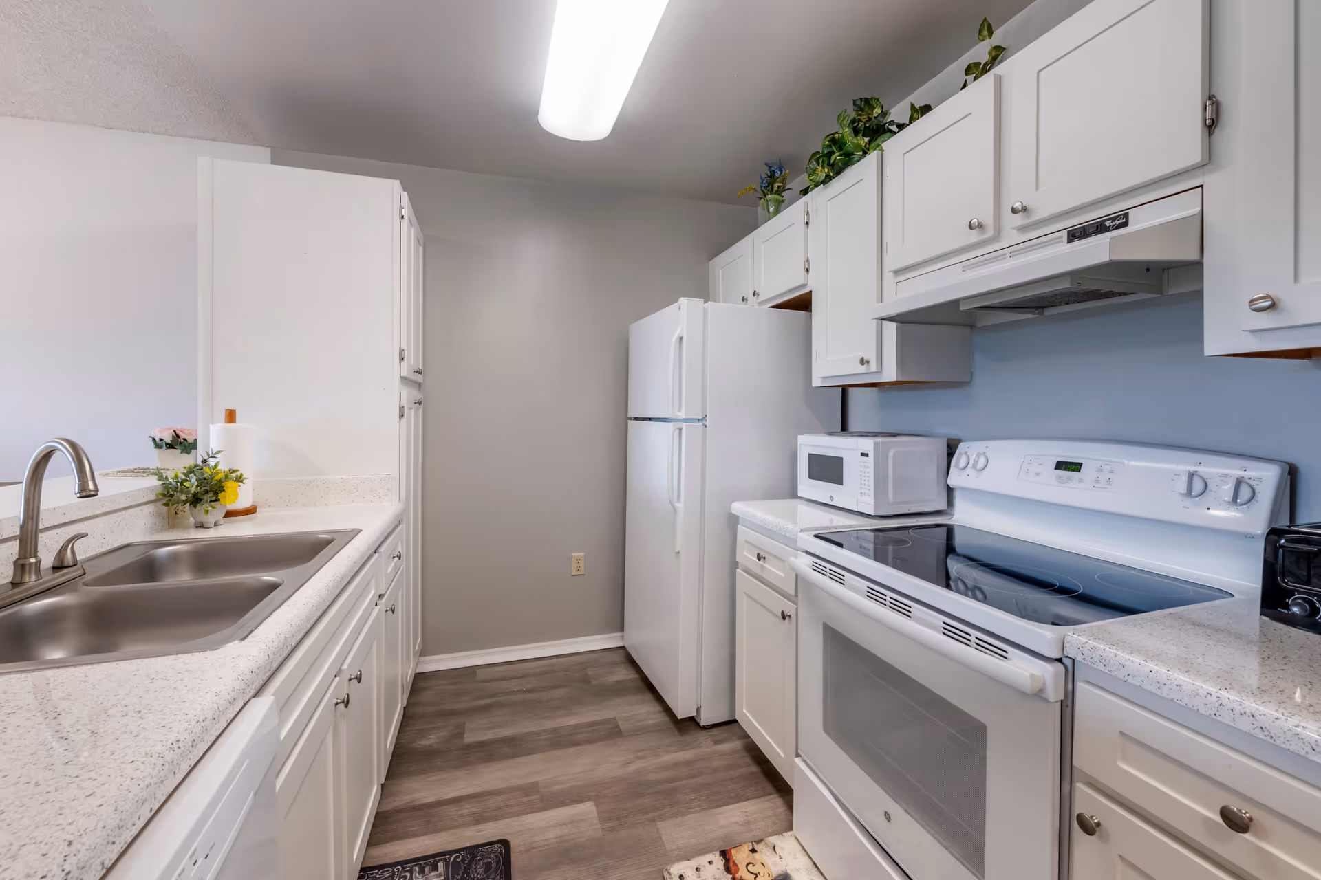 Galley kitchen with white cabinets and countertops, a stainless double sink, white refrigerator and electric range.