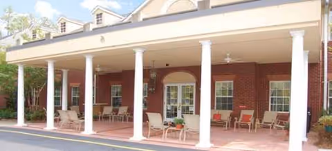 Front porch of a brick senior living facility with white columns and outdoor seating.