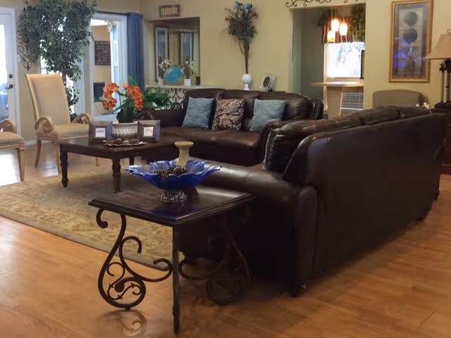 Spacious furnished living room with dark leather sofas, side tables, decorative accents, and wood flooring.