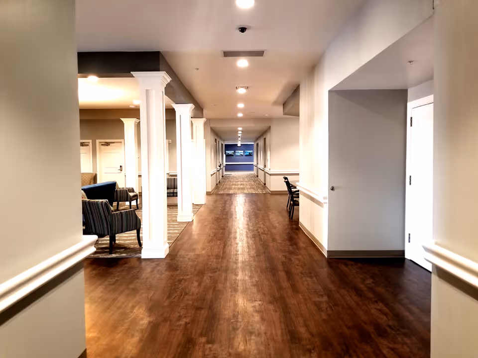 Long, well-lit interior hallway with wood flooring, white columns and seating areas along the left side.
