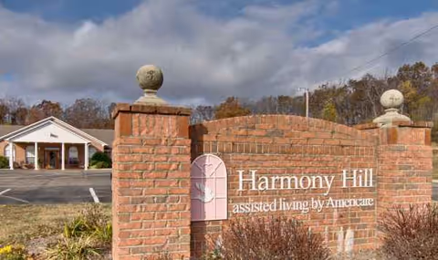 Exterior view of Harmony Hill assisted living sign with brick entrance and building in background.
