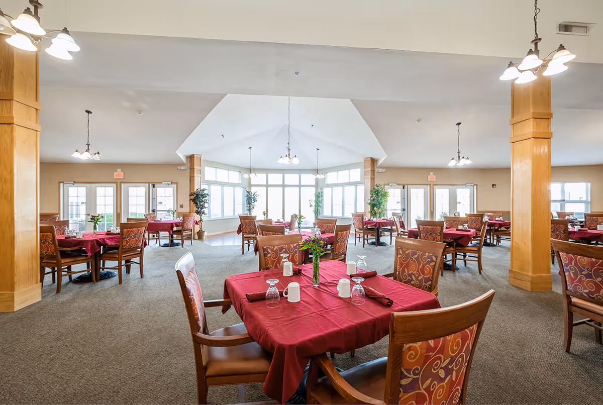 Spacious dining room with tables covered in red tablecloths and chairs arranged under hanging lights.
