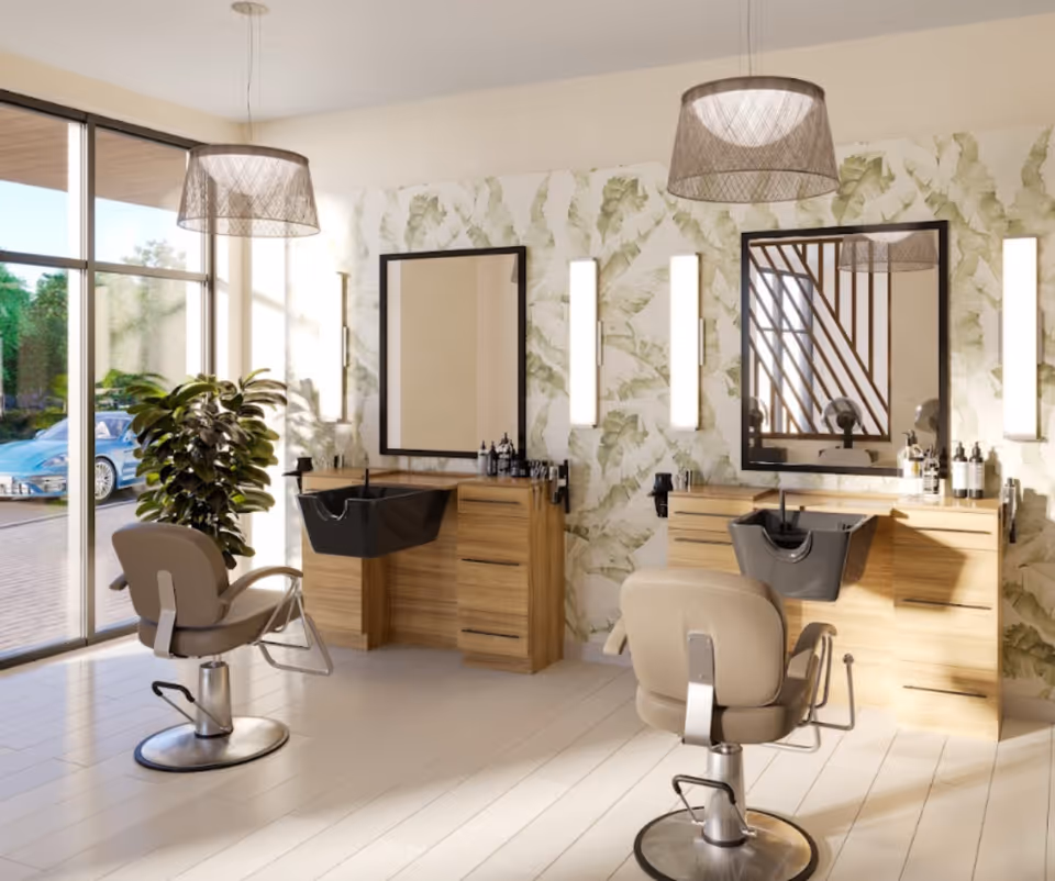 A bright and modern salon area with two beige salon chairs facing wooden counters with black wash basins and large mirrors. The walls have a leafy green wallpaper, and there are vertical light fixtures on either side of the mirrors. A large window on the left side lets in natural light, and a green plant is placed near the window.