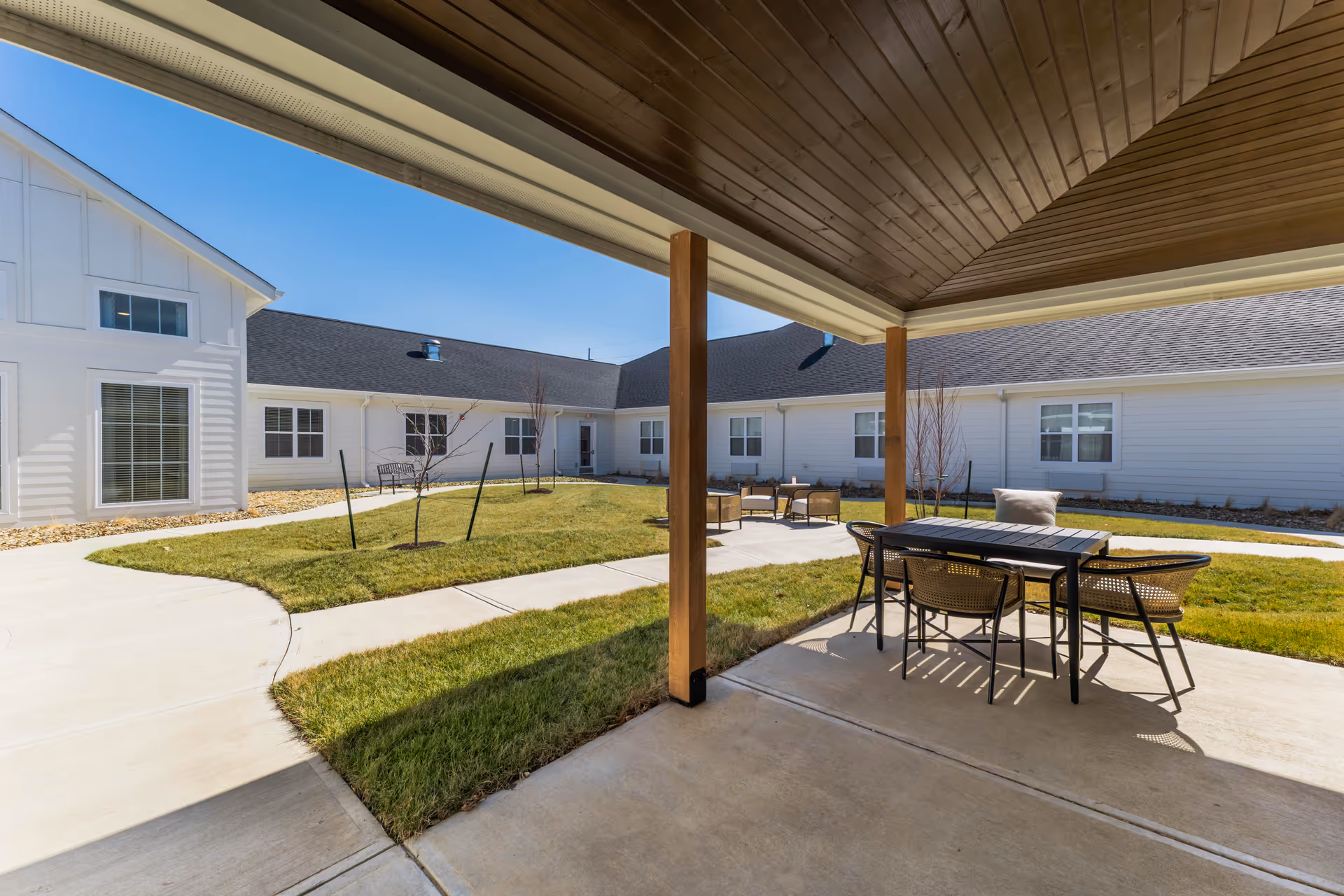 Covered patio overlooking a landscaped courtyard with tables, chairs, walkways, and surrounding single-story building.