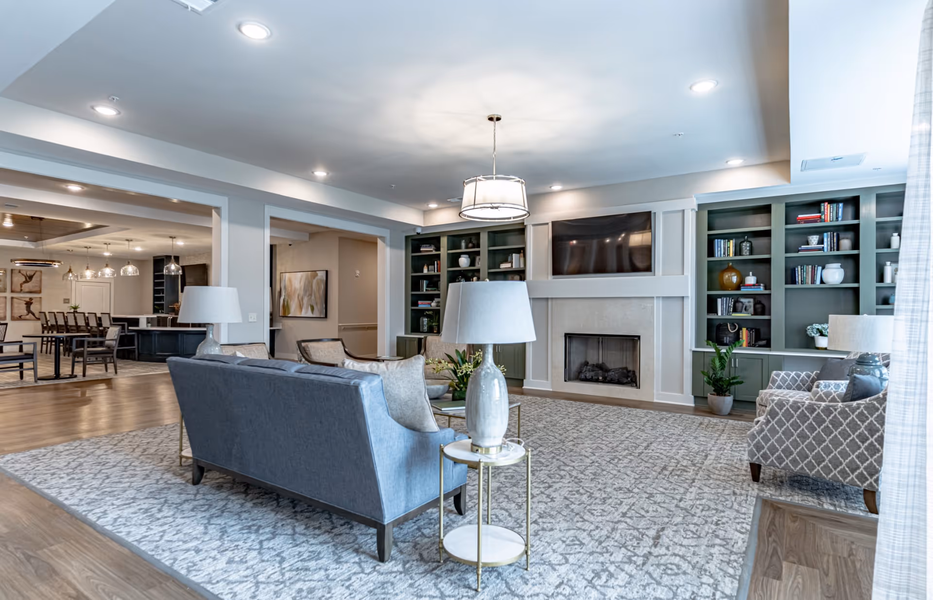 Spacious furnished communal living room with sofas, armchairs, built-in bookshelves, a fireplace and a wall-mounted TV.