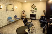 A small salon-style room with swivel styling chairs, shampoo stations, and a row of waiting chairs against patterned wallpaper.