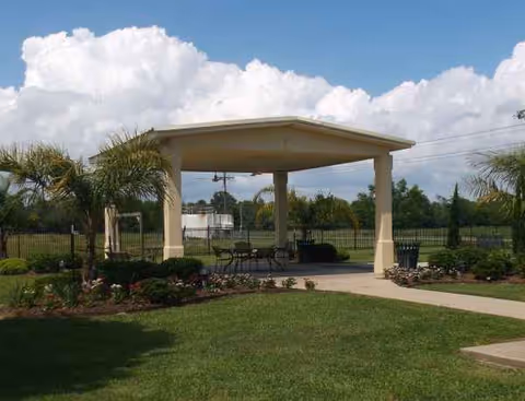 Outdoor pavilion with seating and landscaped garden in a fenced healthcare center yard.