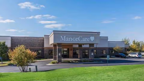 Exterior view of Harmony Utica Ridge ManorCare building entrance with parking and lawn.