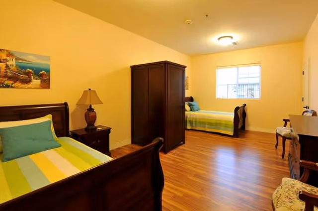 Bright twin bedroom with two wooden sleigh beds separated by a dark armoire, hardwood floors, and a window.
