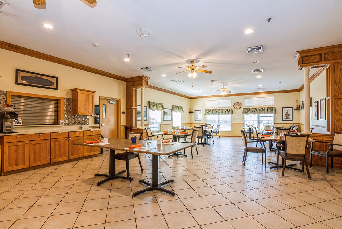 Spacious dining room with multiple tables and chairs, a service counter with wooden cabinets along one wall, ceiling fans, and large windows.
