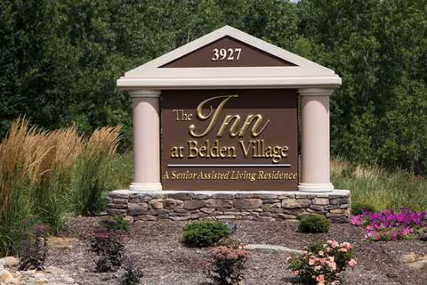 Exterior sign reading The Inn at Belden Village with stone base and landscaping.