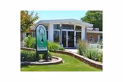 Front view of a small senior living facility with glass doors and a green curved sign.