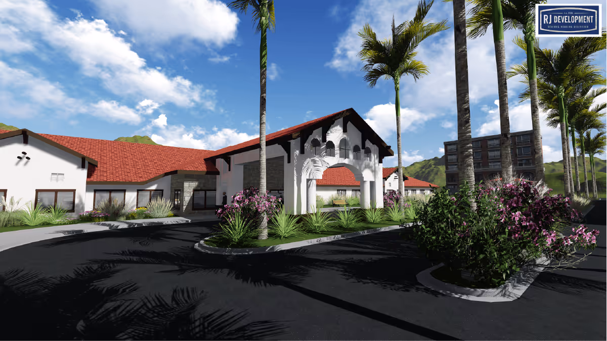 Exterior view of a senior living facility with white walls and red tile roofs, surrounded by palm trees and landscaped greenery under a blue sky with scattered clouds. The building features an arched entrance and a driveway with a roundabout. Mountains are visible in the background.