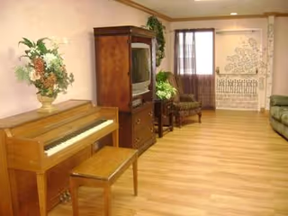 Spacious living room with a piano, TV armoire, seating, plants, and wood floors.