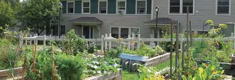 Front of Whitney Hill Homestead building with a fenced community garden and raised beds.