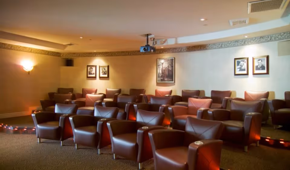 Cozy screening/media room with multiple brown leather recliner chairs arranged in rows facing a ceiling-mounted projector.