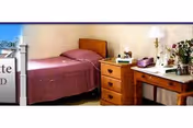 A small bedroom in a senior living facility with a bed, dresser, and desk.