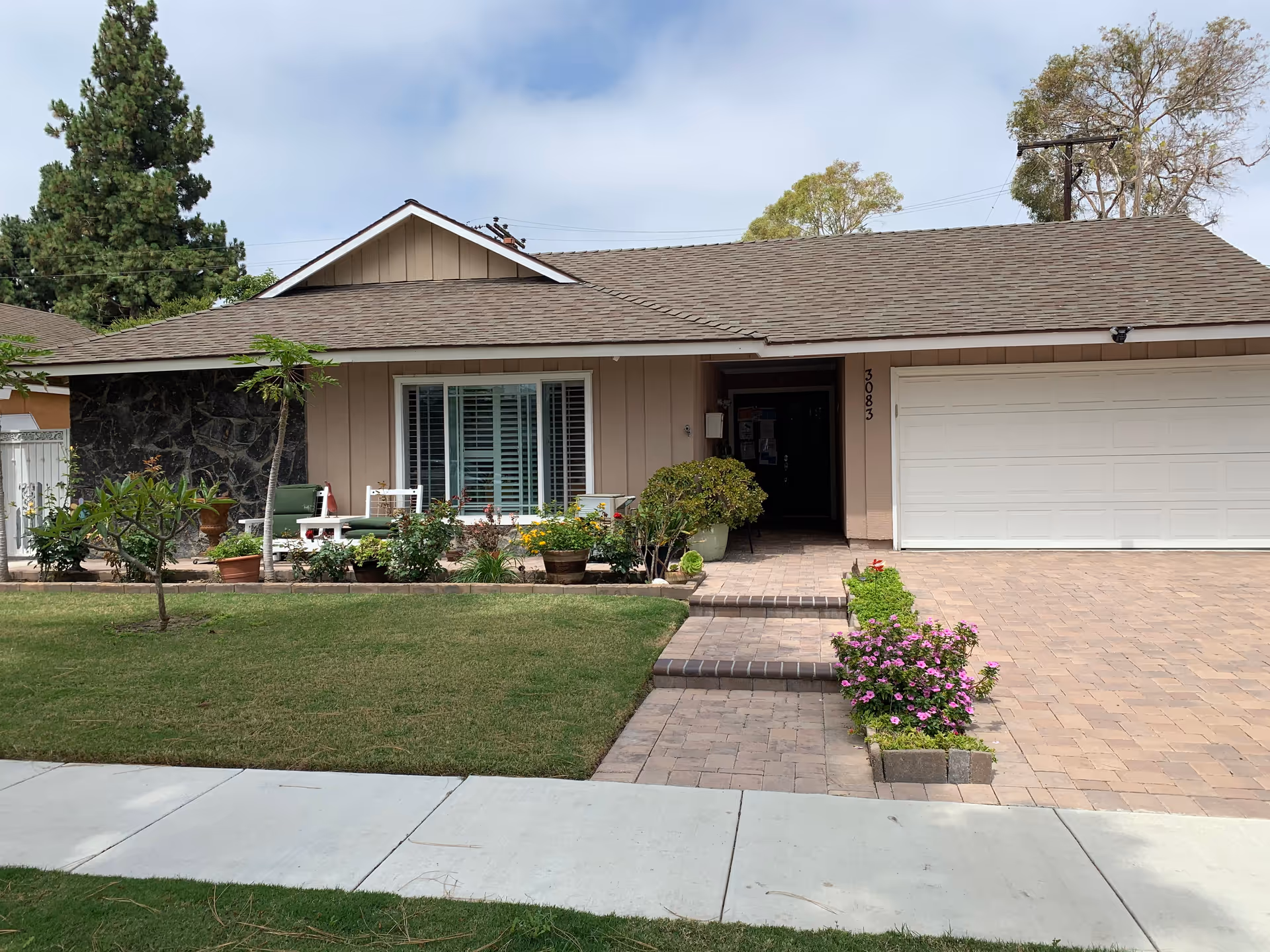 Front exterior of a single-story house with a two-car garage, small porch, lawn and potted plants.