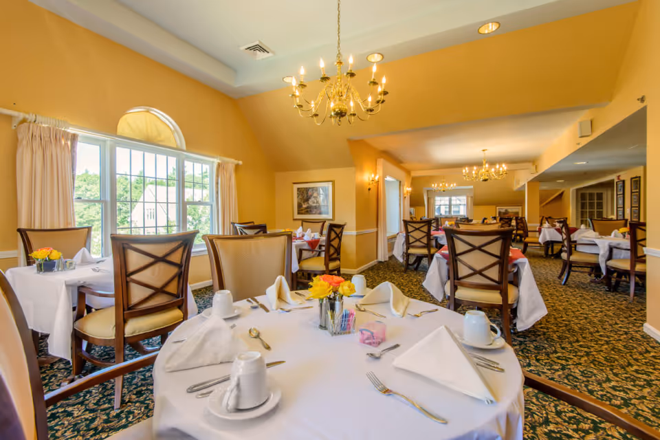 Sunlit dining room in a senior facility with tables set for meals.