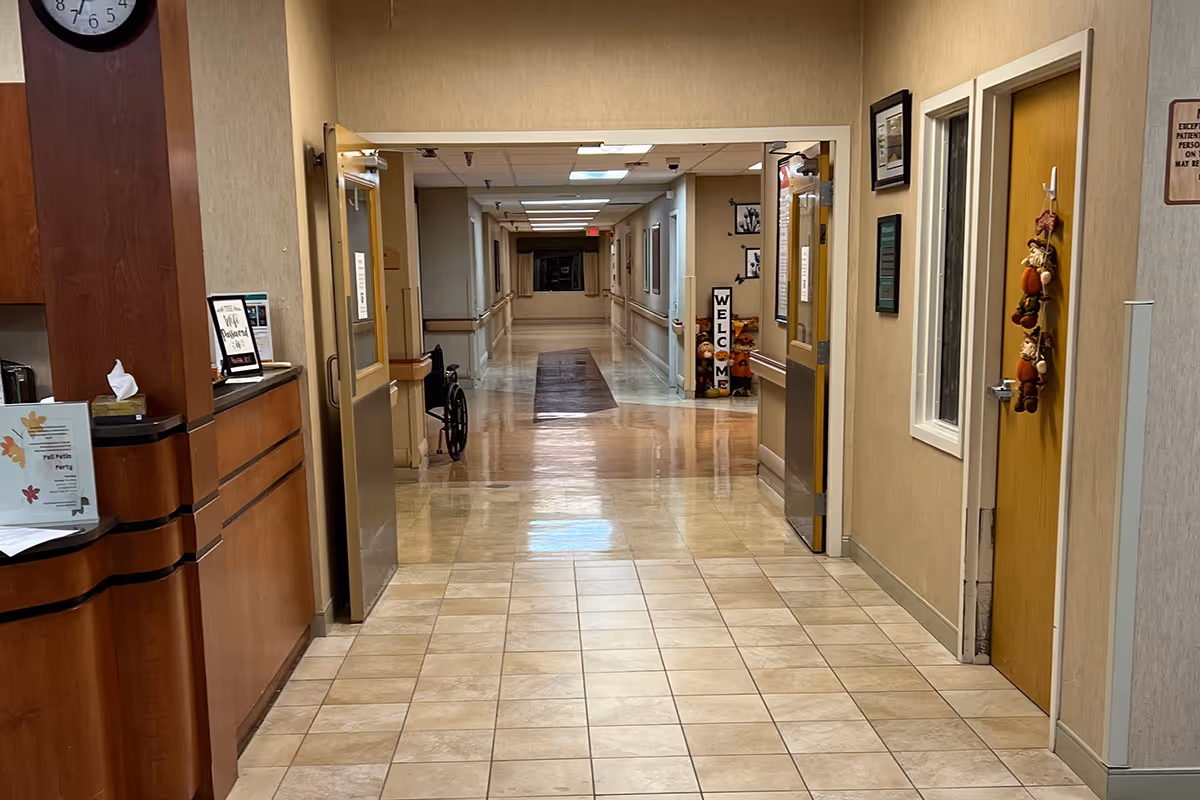 A long beige hallway inside a senior living facility with doors along the walls and a wheelchair near the entrance.