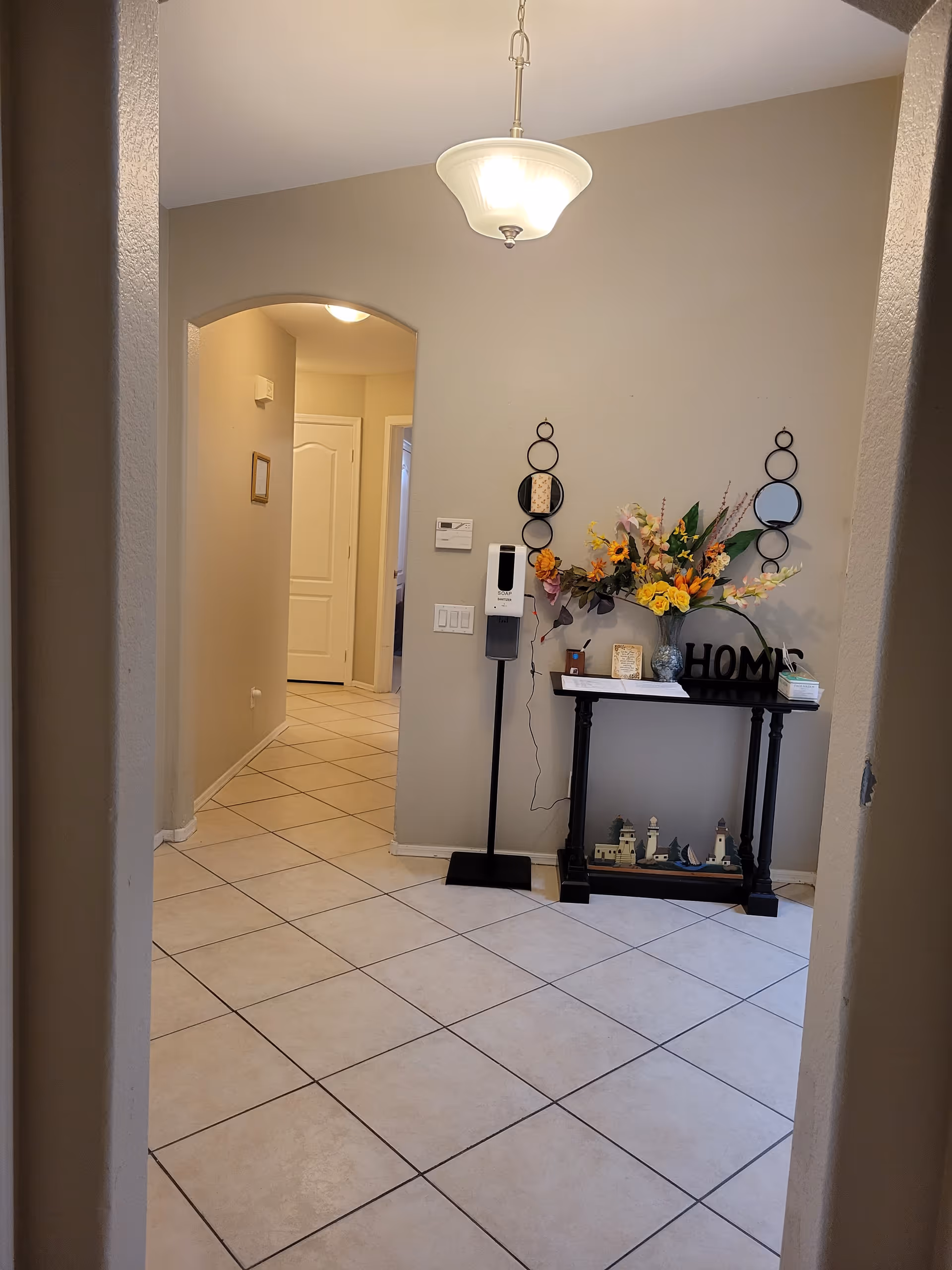 Tiled entry hallway with a console table holding a vase of flowers and decor under a hanging ceiling light.