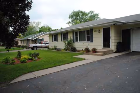 Single-story beige senior living home with a green lawn and driveway.