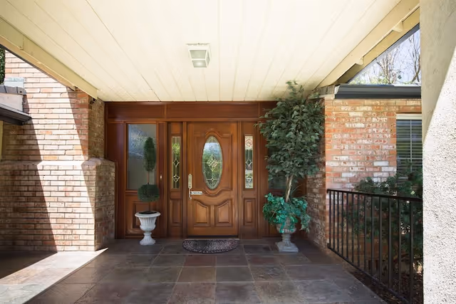 Wooden front door with oval glass, brick facade, potted plants at entrance.