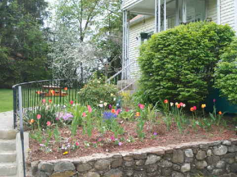 Front garden at Garden Brook with colorful flowers, stone wall, and shrubs beside the porch.