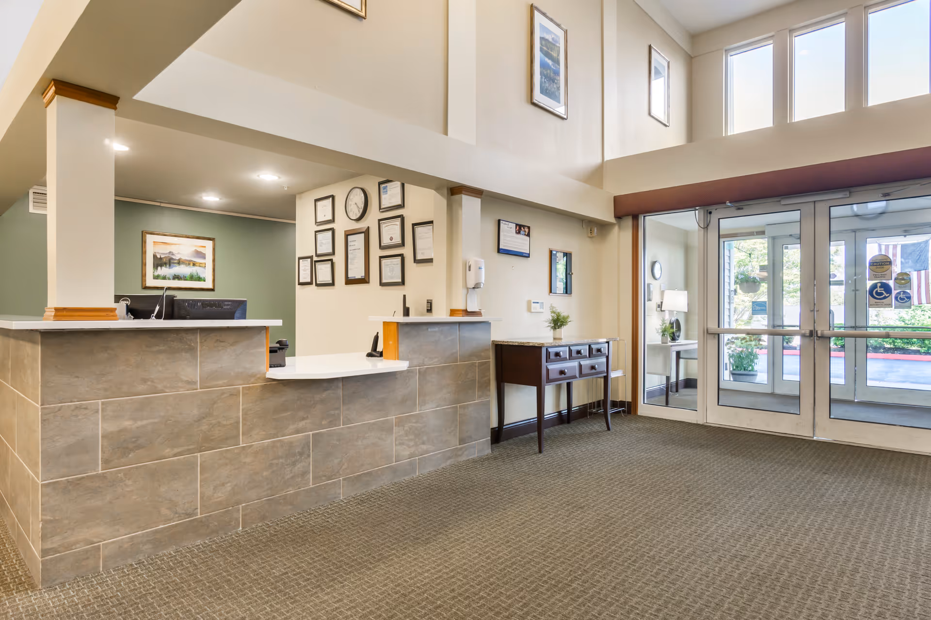 Lobby reception area with a tiled front desk, framed certificates on the wall, and glass entrance doors.