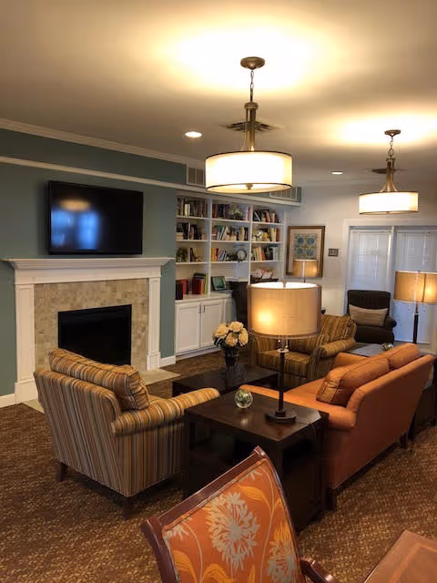 Cozy communal living room with a fireplace and TV, bookshelves, sofas and armchairs, and multiple lamps and pendant lights.