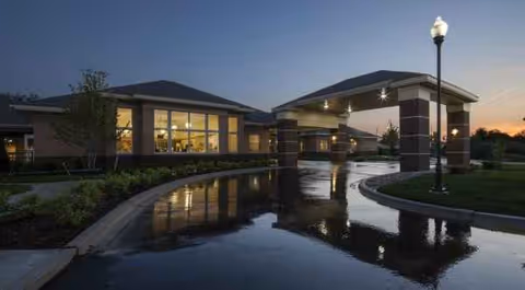 Exterior view of WellBridge of Brighton at dusk, showing the entrance with curved driveway and lights.