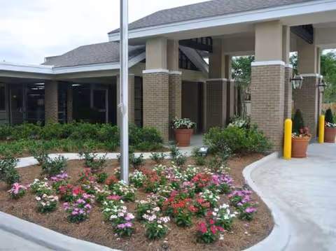 Exterior view of Zachary Manor Nursing and Rehabilitation Center entrance with brick columns and flower beds.