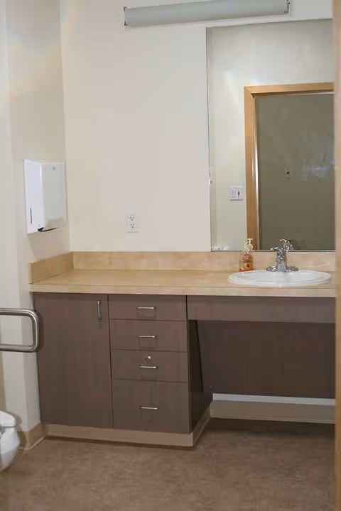 Senior living bathroom with sink, mirror, cabinets, towel dispenser, and grab bar.